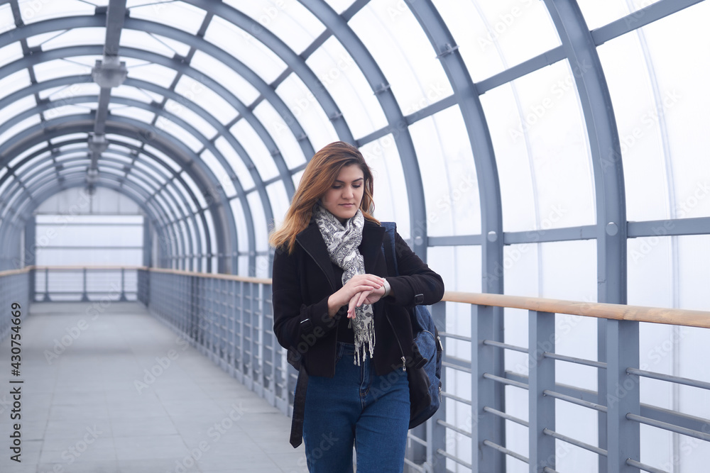 young woman walks along a covered walkway and looks at her watch young woman walks along a covered walkway and looks at her watch