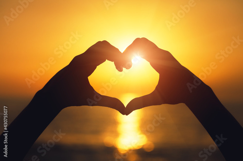 Heart shape hand sign, young woman making heart with two hands against sunset light, love and feelings concept