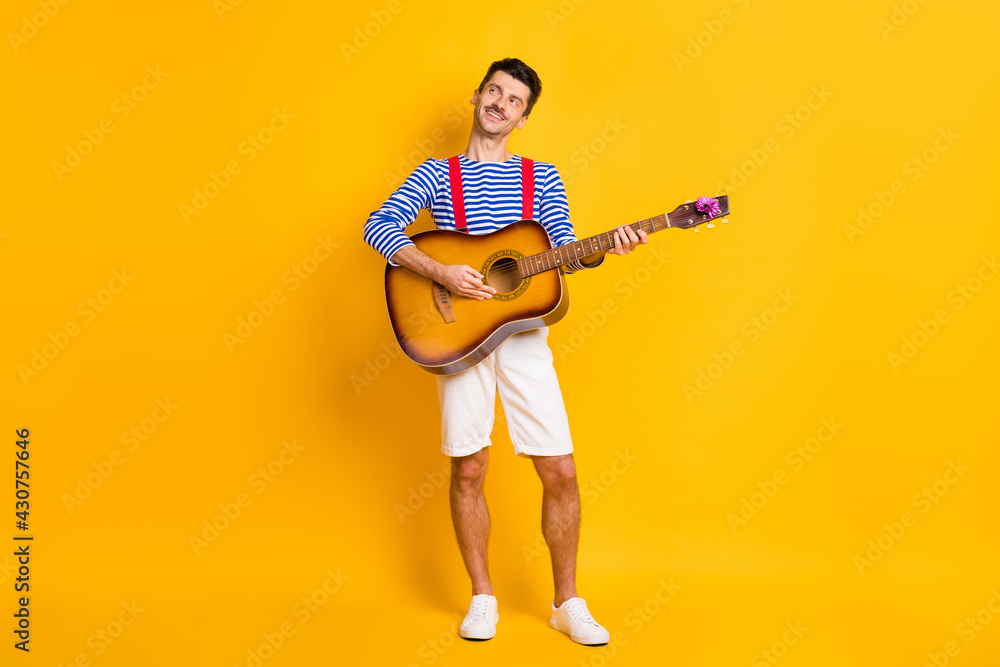 Full size photo of young handsome happy positive smiling dreamy man playing guitar isolated on yellow color background