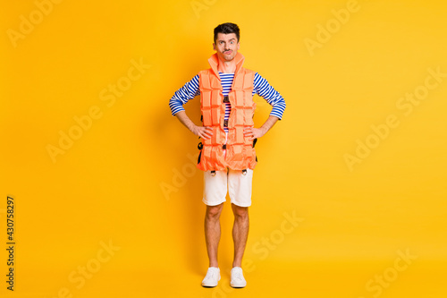 Full size photo of serious young man hold hands waist wear lifeguard vest isolated on yellow color background © deagreez
