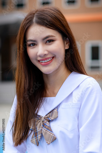 Cute and young girl wearing Japanese, Kerean style schoolgirl uniform pose to camera with fun and happy in front of school building photo