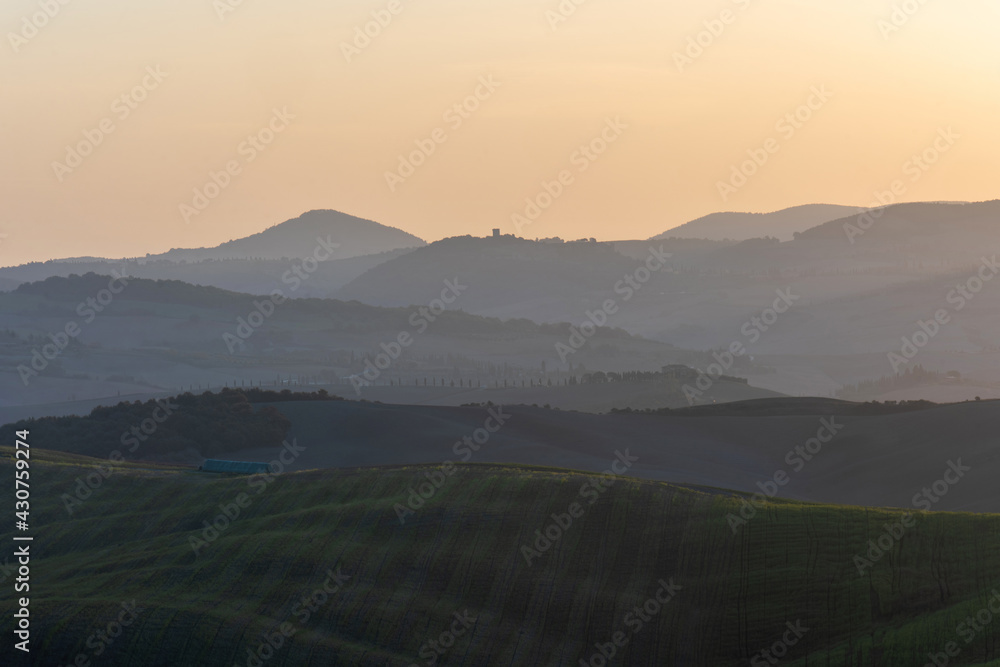 Fototapeta premium A stunning landscape view on an autumn morning of the hills of Tuscany with ploughed and green grass covered with beautiful undulating fields. The sunlight covering the meadows and fields makes
