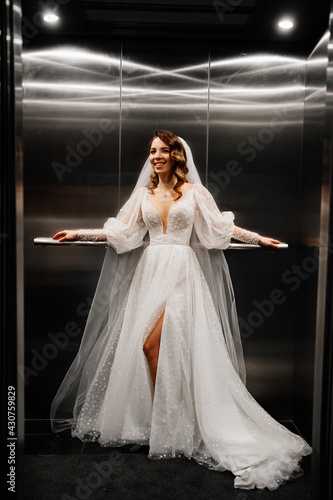 bride in a white elegant dress  with a long veil stands in a dark lift.