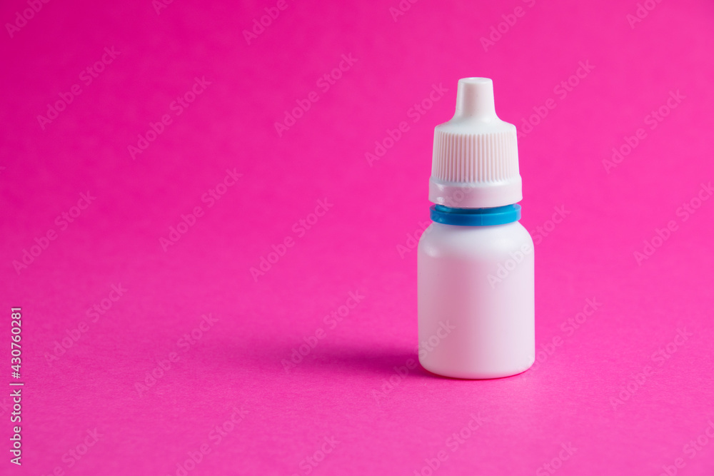 White bottle with nose or eye drops on a pink paper background. Medicine on background with copy space. White bottle with nose or eye drops on a pink paper background. Medicine on background with copy space.