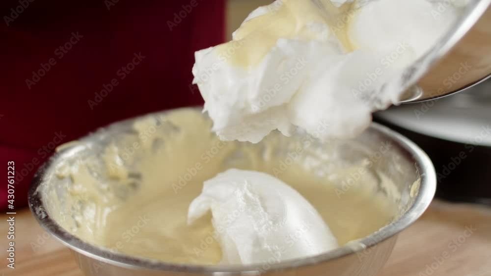A male chef mixes whipped egg whites and yolks with flour in an iron bowl to create a biscuit dough A male chef mixes whipped egg whites and yolks with flour in an iron bowl to create a biscuit dough