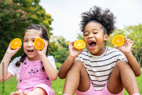 Two African American little girl sitting on the mat and eating oranges fruits in the autumn park , play with oranges fruits