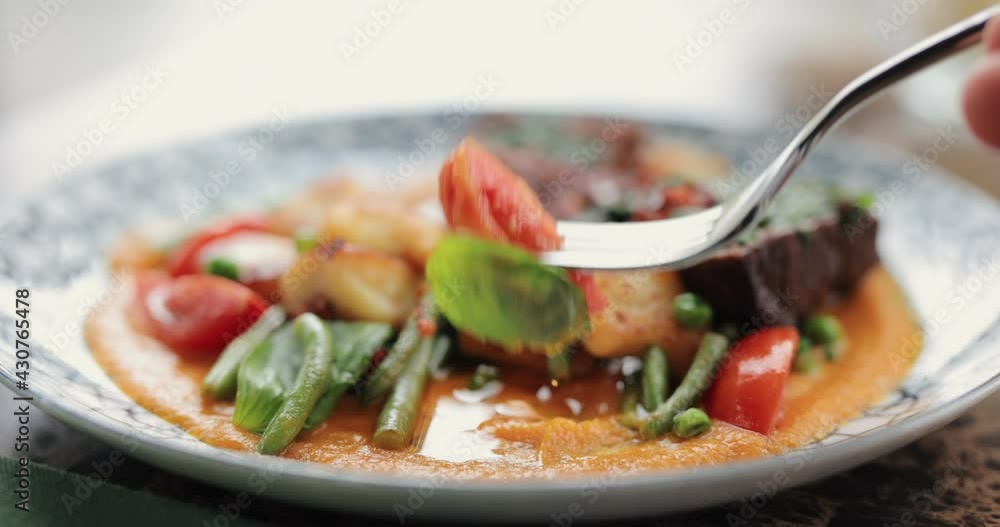 Eating restaurant food from the plate close up, meal and vegetables, prick tomato with a fork Eating restaurant food from the plate close up, meal and vegetables, prick tomato with a fork