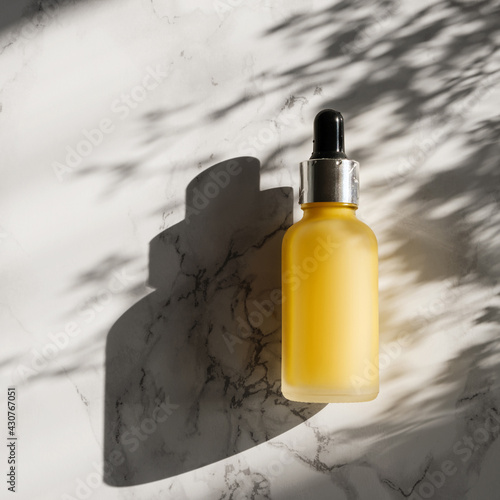A bottle of a Vitamin C serum on a marble background with a harsh shadow.