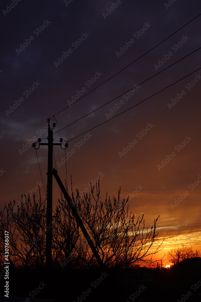 Black silhouette of a pillar and trees against a dark orange sunset sky