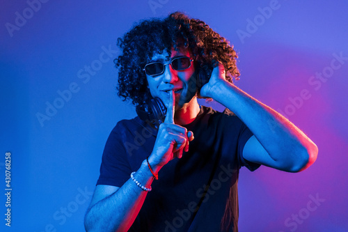 Young beautiful man with curly hair is indoors in the studio with neon lighting