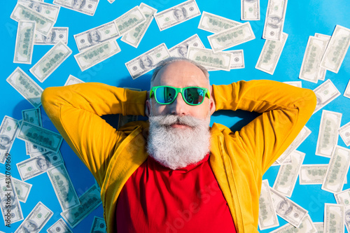 High angle view photo of happy good mood positive grandfather in sunglass lying floor with money isolated on blue color background photo