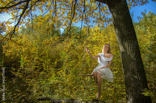 The girl is swinging on a swing in the autumn forest against the background of yellow-gold foliage. Selective focus.