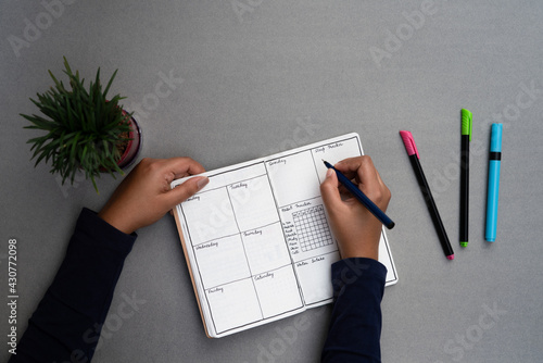 Journaling daily for mental well being and personal development. Weekly planner set up on a minimal grey table top, with sketch pens and a green house plant