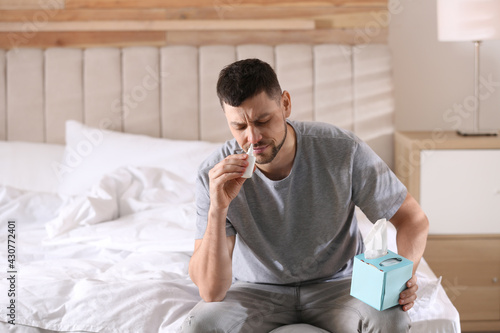 Ill man with nasal spray and box of tissues on bed at home