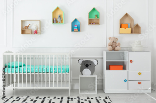 Comfortable crib near wall with color shelves in baby room. Interior design © New Africa