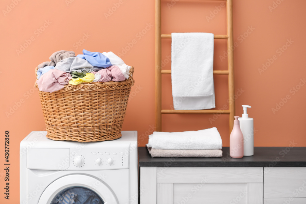 Wicker basket with dirty laundry on washing machine near coral wall indoors Wicker basket with dirty laundry on washing machine near coral wall indoors
