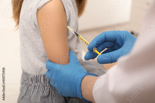 Doctor giving injection to little girl in hospital, closeup. Immunization concept