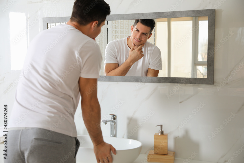 Handsome man touching his smooth face after shaving near mirror in bathroom Handsome man touching his smooth face after shaving near mirror in bathroom