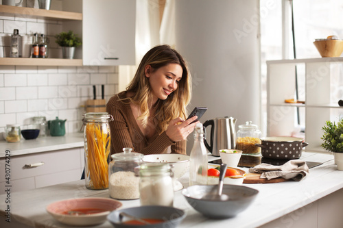 Attractive woman cooking in modern kitchen. Beautiful woman using the phone while preparing delicious food