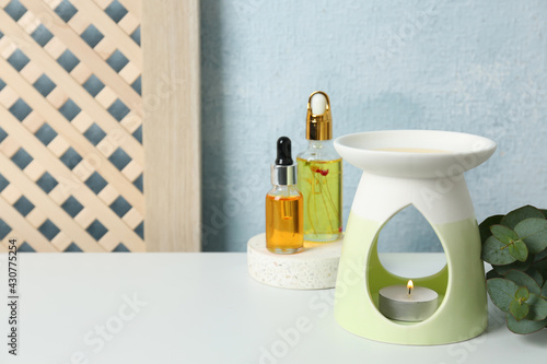 Aroma lamp and essential oils on white table. Space for text photo