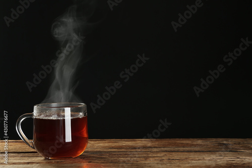 Cup with steam on wooden table against black background. Space for text