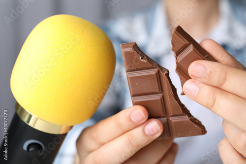 Woman making ASMR sounds with microphone and chocolate, closeup photo