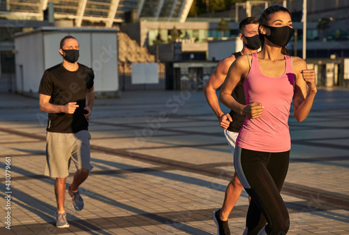 Three athletes in protective masks on their faces while jogging