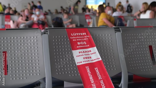 Airport, seats for passengers in departure terminal with Red and White Lines of barrier tape. Coronavirus COVID-19. People travelers tourists in airport check-in for flight boarding plane in face mask