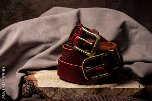 Red and orange belt with gold buckles lie on a wooden cut on a brown background close-up