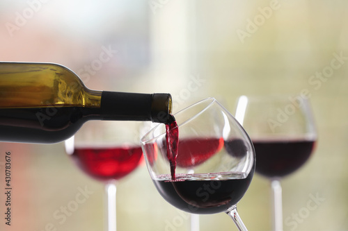 Pouring red wine from bottle into glass on blurred background, closeup