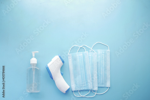 Surgical masks, thermometer and hand sanitizer on blue background 