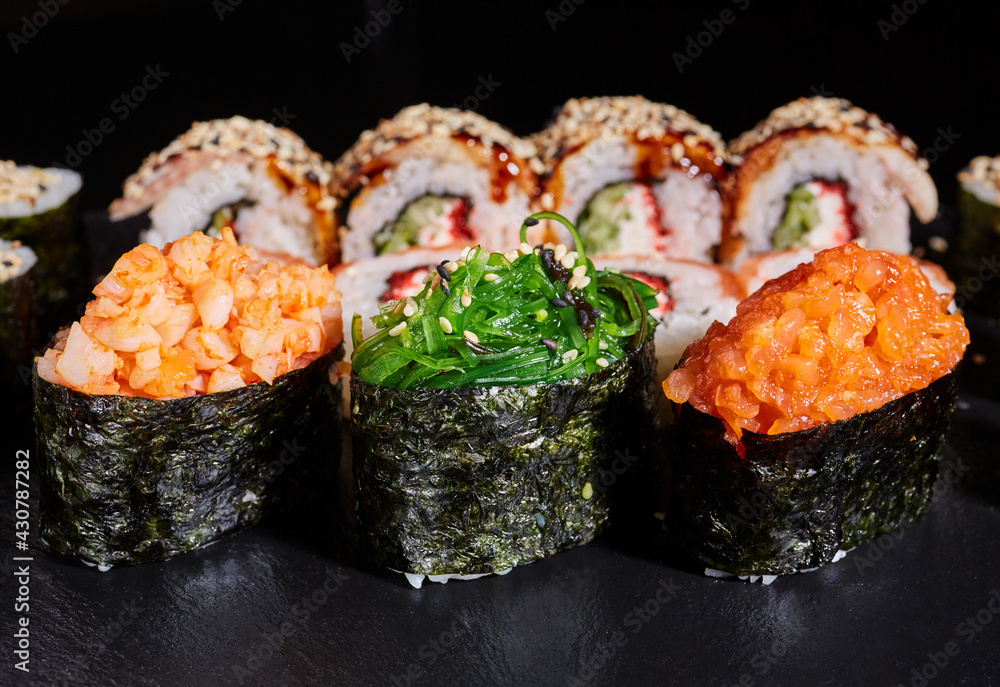 Sushi rolls with seaweed, shrimp, salmon and sprinkled with sesame seeds on a black board. Sushi rolls with seaweed, shrimp, salmon and sprinkled with sesame seeds on a black board.