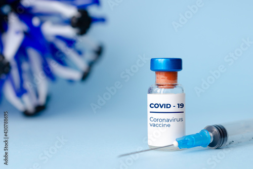 Ampoules in hand and syringe with Covid-19 vaccine on blue background. For the prevention, immunization and treatment of coronavirus infection.Infectious medicine concept. With copy space