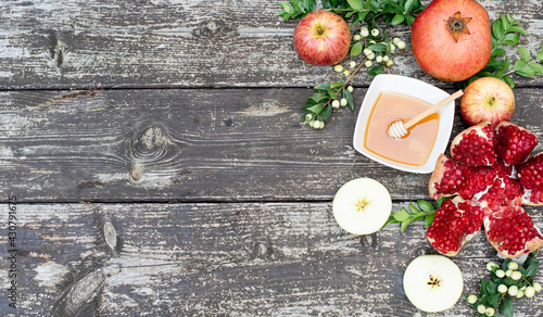 Beautiful layout of traditional symbols for jewish holiday - apples, cup with honey, pomegranate, green branch on wooden background. Concept Rosh Hashanah tova jewish New Year. Banner, fresh fruits