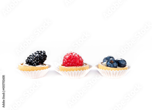 A group of mini tarts with berries isolated, delicious tiny cakes on white background,  small blueberry and raspberry cakes, sweet mini pies, gourmet dessert close-up 