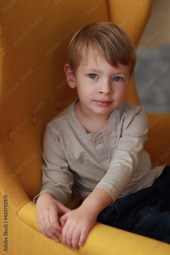 Little blond boy on the yellow armchair. International Children's Day