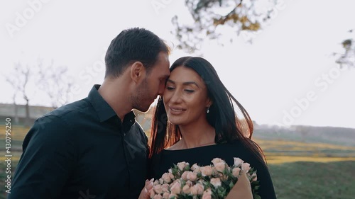 Happy young people fall in love under the sunset and keep themselves happy glued to each other. She happily cried a large bouquet of flowers, and he looked at her in love