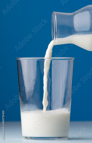 glass of milk half full, with glass bottle, blue background