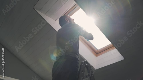 Caucasian man washes the attic window Bright sun illuminates the man in the window during the repair The husband performs finishing work in the house Happy family