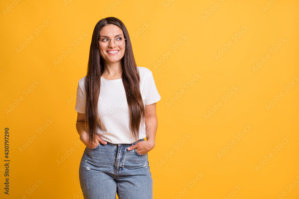 Photo of attractive cheerful lady look stand empty space hold hands pockets good mood isolated on yellow color background Photo of attractive cheerful lady look stand empty space hold hands pockets good mood isolated on yellow color background
