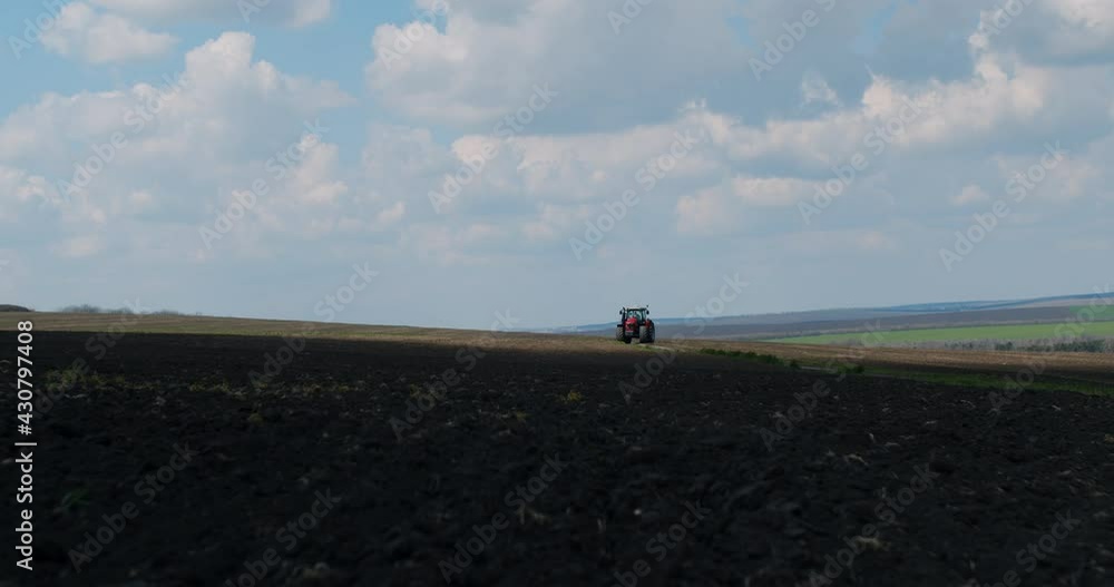 A modern and red tractor on the agricultural field. A farmer on the hills. A modern and red tractor on the agricultural field. A farmer on the hills.