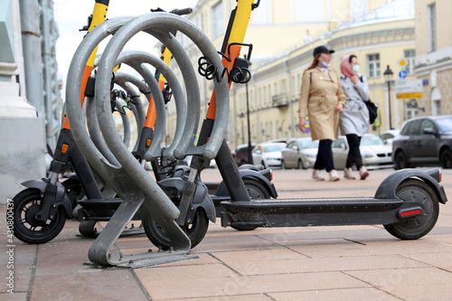 Electric scooters in a row on the parking lot on walking people background. City bike rental system, public e-scooters on the street