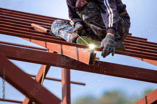 Wallpaper Mural Red painted steel roof truss, with roof welders working at dangerous heights. Welding of steel is very technically demanding and is only professional. Bright sky background Torontodigital.ca