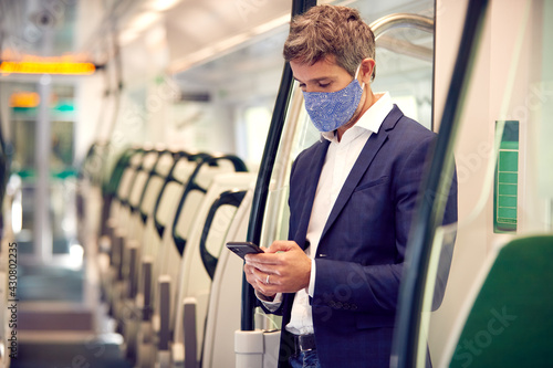 Businessman Stands In Train Carriage Using Mobile Phone Wearing PPE Face Masks During Pandemic