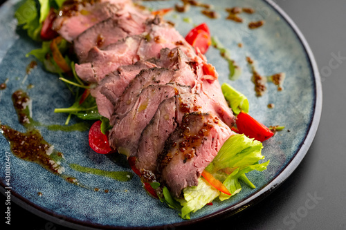 Grilled duck meat with salad on a grey plate on a black background.