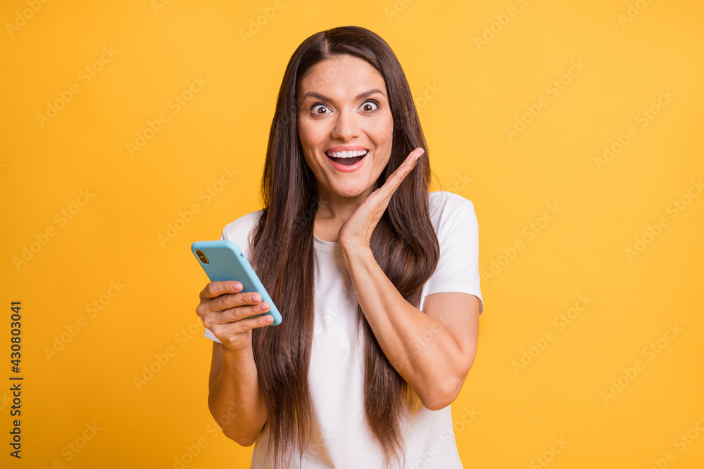 Photo portrait of pretty woman amazed holding mobile phone staring palm near face surprised isolated on bright yellow color background Photo portrait of pretty woman amazed holding mobile phone staring palm near face surprised isolated on bright yellow color background