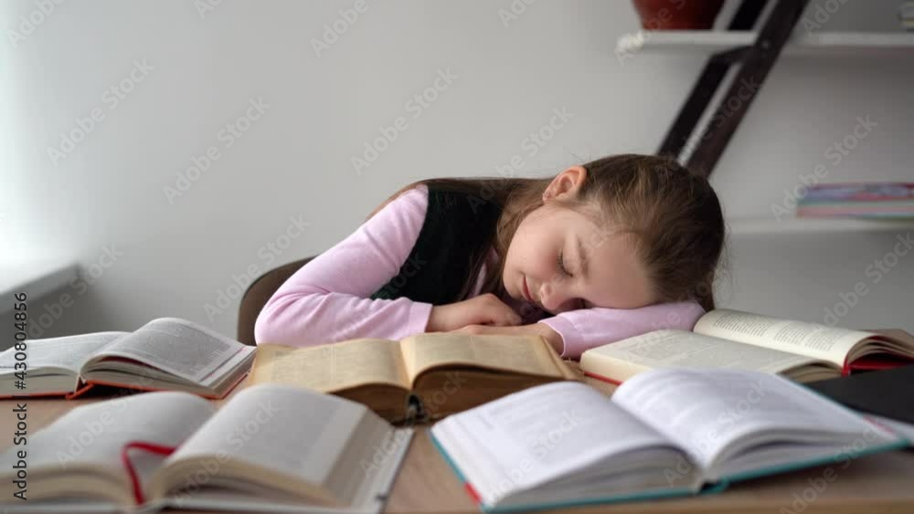 Sleepy tired unmotivated student lying at a desk with open books studying the material of several lessons at the same time. Smart child wunderkind reads literature while studying online at home. Sleepy tired unmotivated student lying at a desk with open books studying the material of several lessons at the same time. Smart child wunderkind reads literature while studying online at home.
