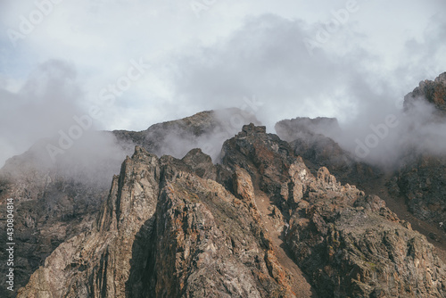 Scenic mountain landscape with great rocks in cloudy sky in vintage colors. Awesome sunny scenery with low clouds on rocky mountain top in pastel tones. Beautiful brown rock in sunlight and low clouds