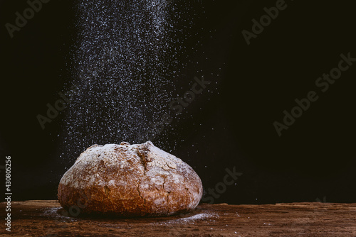 Murais de parede rustic and golden round loaf of fresh whole grain bread on dark black background