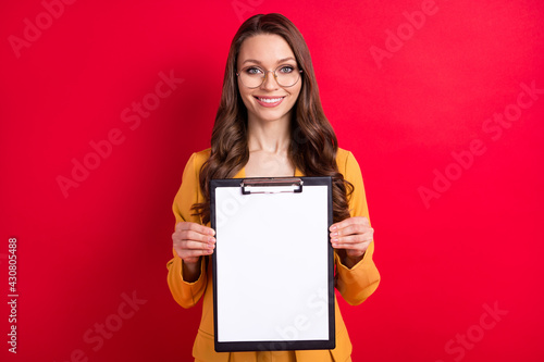 Photo of shiny positive young woman wear yellow jacket spectacles holding empty space documents isolated red color background